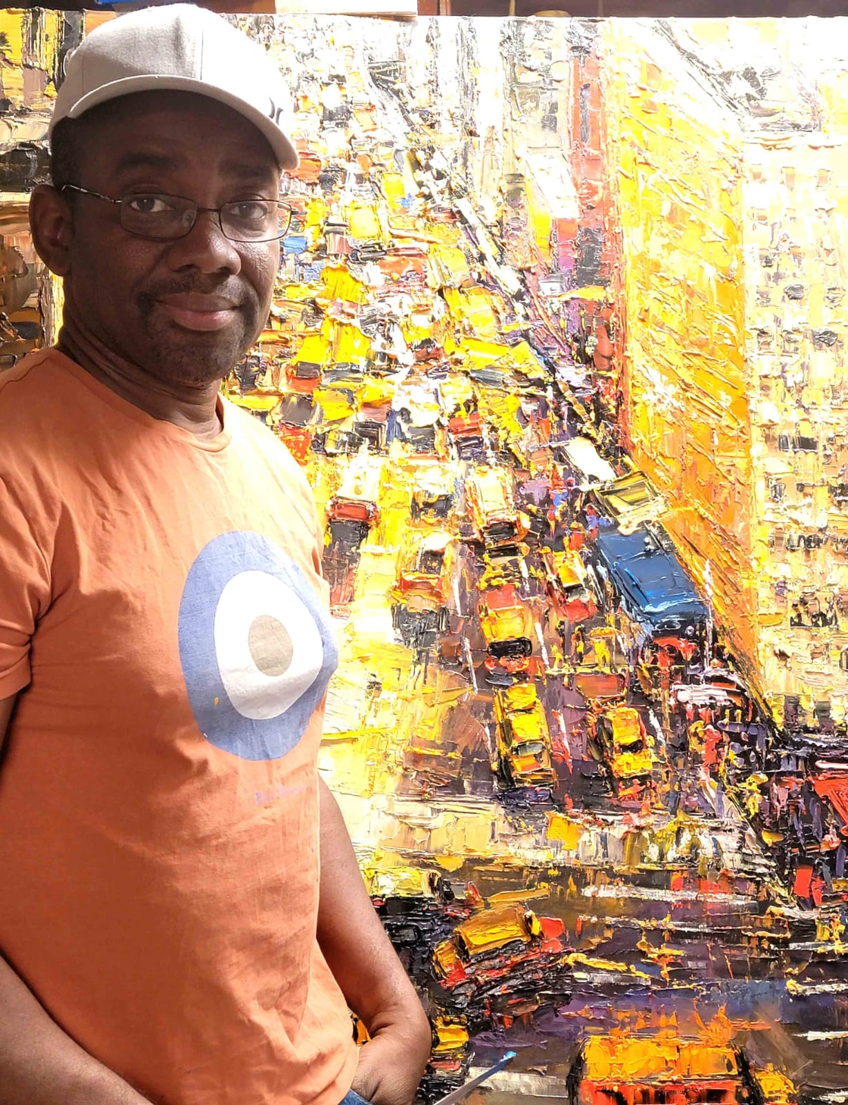 Man in orange t-shirt standing next to a vibrant, colorful abstract painting.