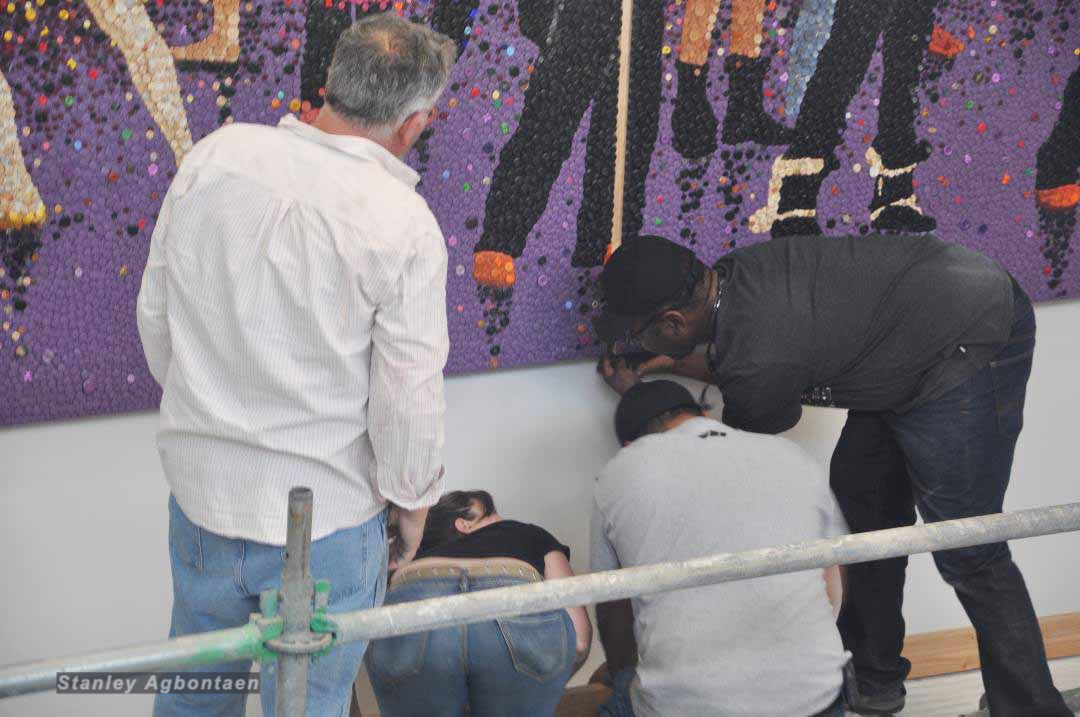 Three individuals installing or examining an artwork on a gallery wall.