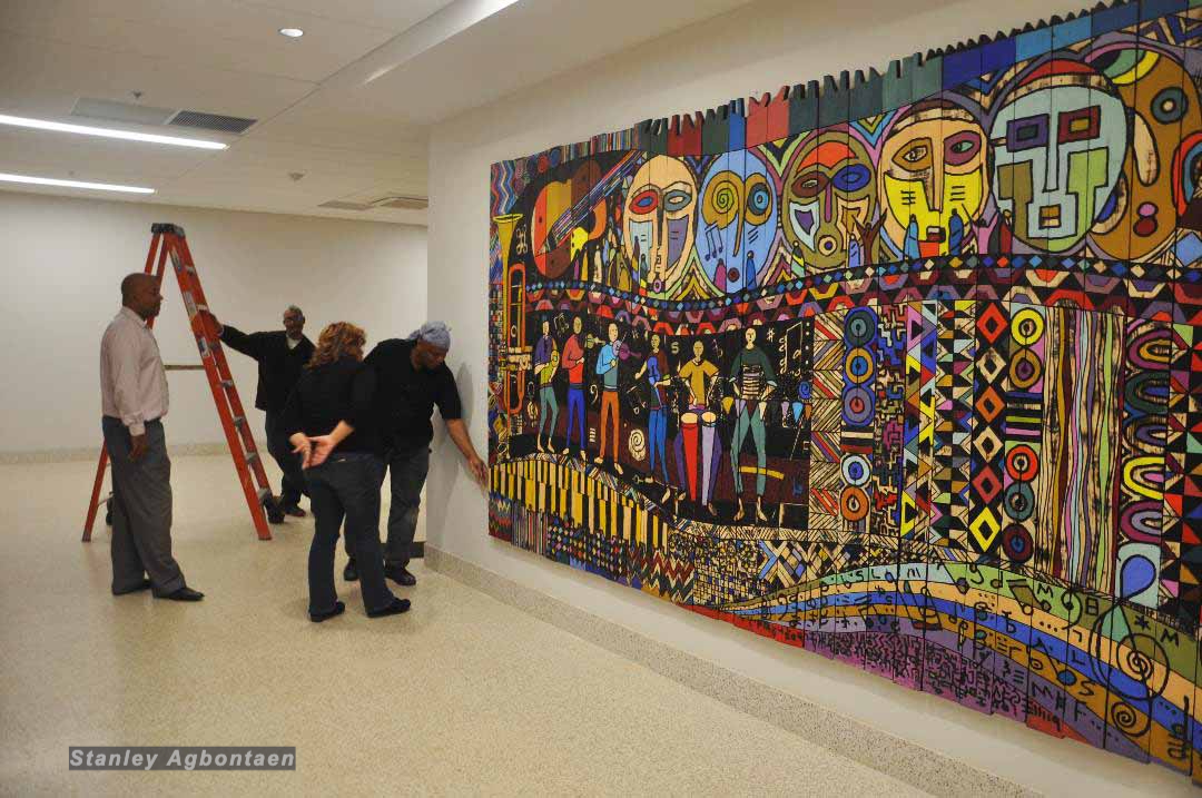 Gallery visitors observe a vibrant, large-scale, colorful mural with abstract figures and patterns.