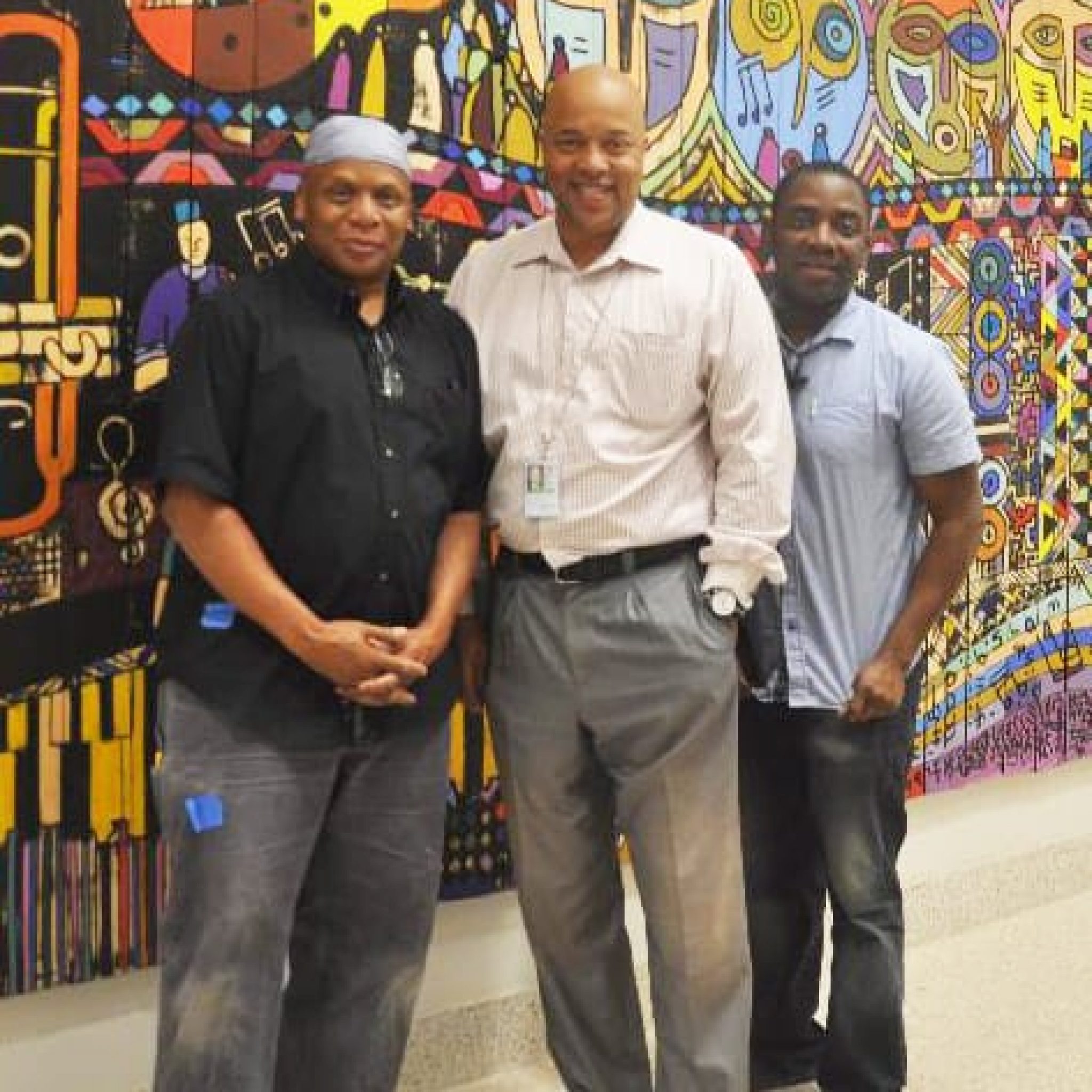 Three individuals standing in front of a colorful mural, smiling for the photo.