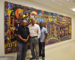 Three men standing in front of a colorful mural in a school in Washington DC.